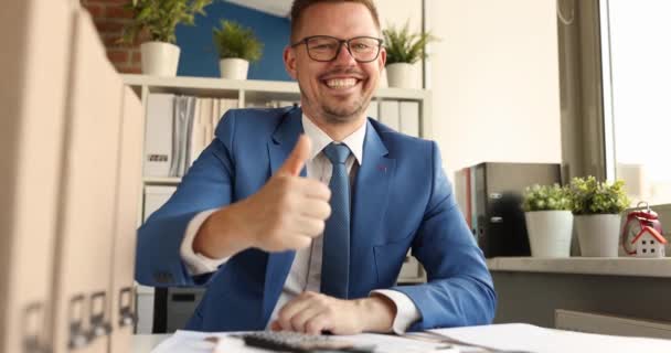 Молодий усміхнений бізнесмен сидить за столом і показує великий палець вгору 4k фільм — стокове відео