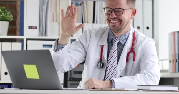 Docteur agitant la main à l'écran de l'ordinateur portable et menant une consultation en ligne au patient film 4k — Video