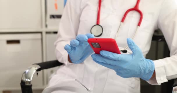 Doctor in medische handschoenen typt tekst op smartphone scherm in kliniek 4k film — Stockvideo