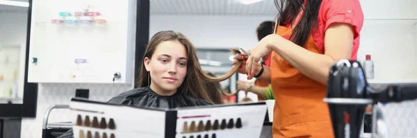 Giovane donna seduta in sedia parrucchiere e tenendo nel suo catalogo mani con tavolozza di colori per la tintura dei capelli — Foto Stock