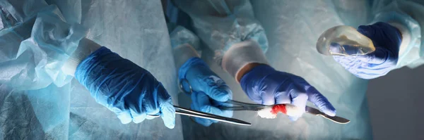 Médicos cirujanos en abrigos protectores que sostienen instrumentos e implantes mamarios en quirófano —  Fotos de Stock