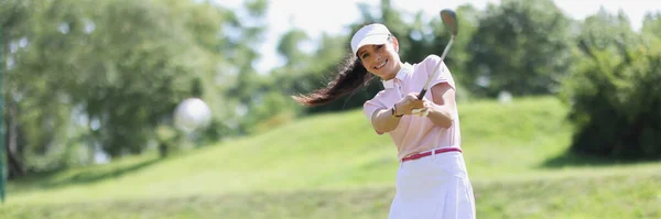 Spor üniformalı genç bir kadın golf sahasında demirle topa vuruyor. — Stok fotoğraf