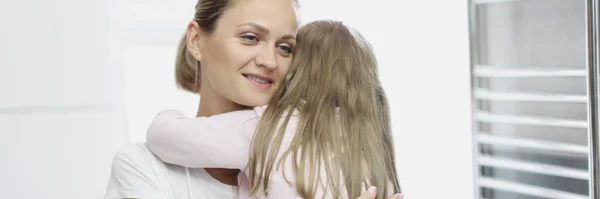 Giovane donna che tiene piccola figlia tra le braccia e abbraccia strettamente a casa — Foto Stock