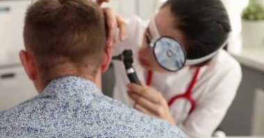 Alnında ön yansıtıcı olan Otorhinolaryngologist hasta kulak otoskobu 4K filmini inceliyor.