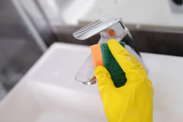 Egy kéz a kesztyűben lemossa a csapot a fürdőszobában egy szivaccsal. — Stock Fotó