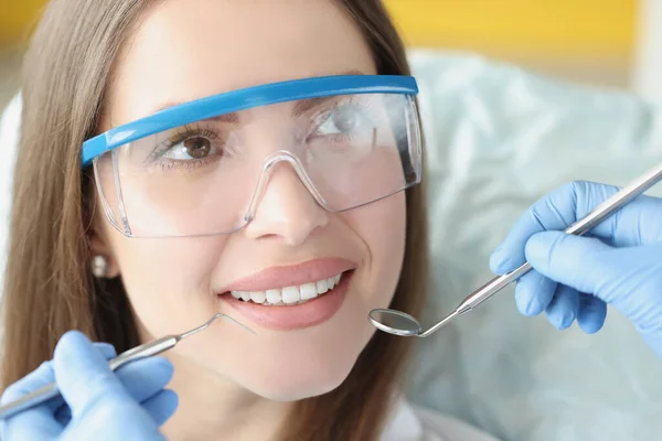 Médico dentista sosteniendo instrumentos médicos frente a un paciente sonriente en la clínica — Foto de Stock