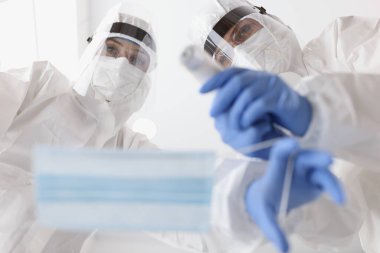 Koruyucu giysili doktor hasta maskesi takıyor ve alttaki sıcaklığı ölçüyor.