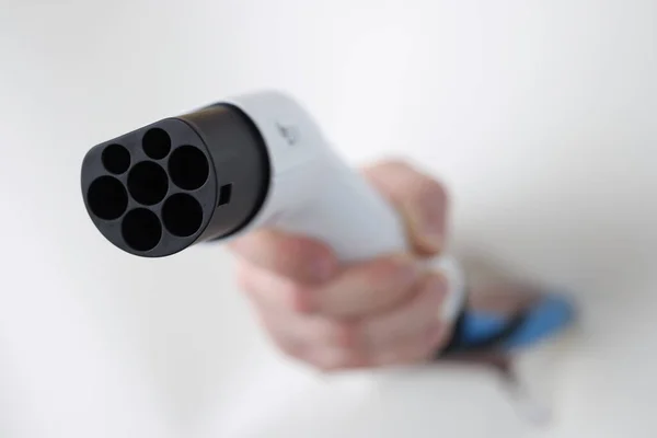 Człowiek ręka trzyma elektryczny przewód ładowania samochodu przez otwór papieru zbliżenie — Zdjęcie stockowe