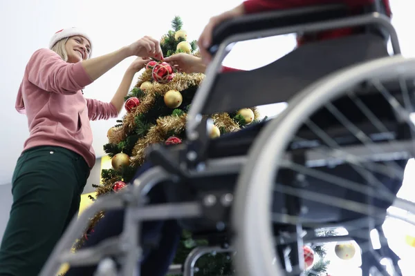 Жінка і друг в інвалідному кріслі висить червоний різдвяний м'яч на новорічній ялинці — стокове фото