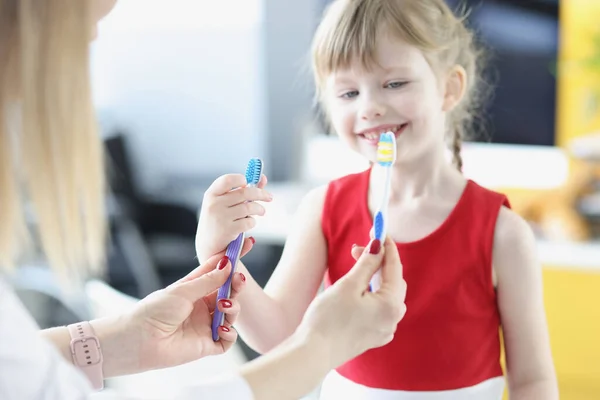 Врач-дантист держит две зубные щетки перед маленькой девочкой крупным планом — стоковое фото