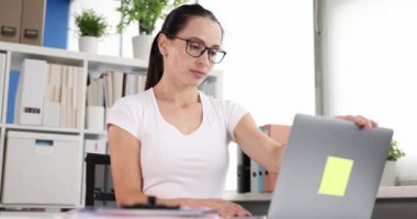 Yorgun kadın dizüstü bilgisayarı kapatıyor ve ofis 4K filminde gözlüklerini çıkarıyor.