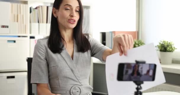 Mulher blogueira explicando informações sobre papel com gráficos na frente da câmera e mostrando polegares até filme 4k — Vídeo de Stock