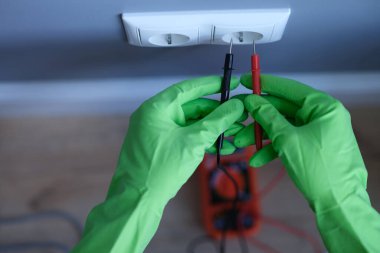 Lastik eldivenli bir zanaatkar evdeki elektrik prizinin yakınında test cihazı tutuyor.