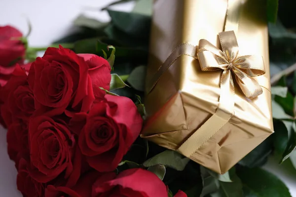 赤いバラの花束の上に横たわる弓と金のパッケージにギフトを閉じる — ストック写真