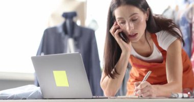 Kadın terzi telefon ile siparişi kabul ediyor ve kağıt 4K film üzerinde yazıyor.