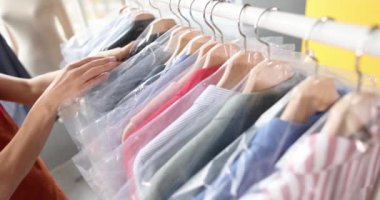 Kadın terzi 4K filminde plastik poşetlerle elbise asıyor.