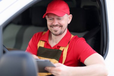 Erkek kurye arabada oturmuş teslimat adresine bakıyor.