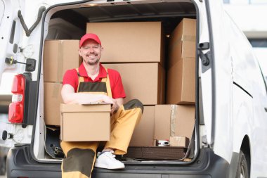Adam kurye kamyonda otururken bir paket tutuyor.
