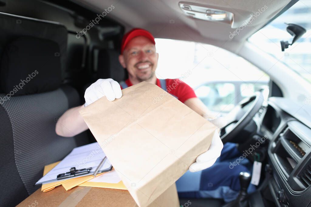 Joyful male courier giving a box while sitting in the car