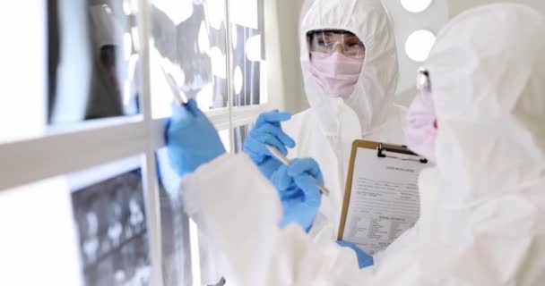 Два врача в защитных костюмах в масках и очках изучают рентгеновские снимки пациентов 4К фильма — стоковое видео