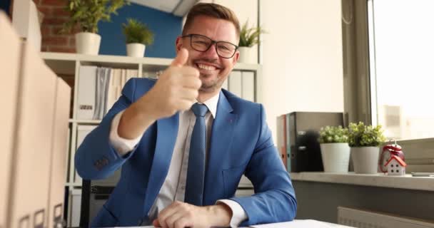 Biznesmen w okularach siedzący przy stole i pokazujący kciuk w górę 4k film — Wideo stockowe
