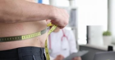 Adam doktor randevusunda belini bantla ölçüyor.