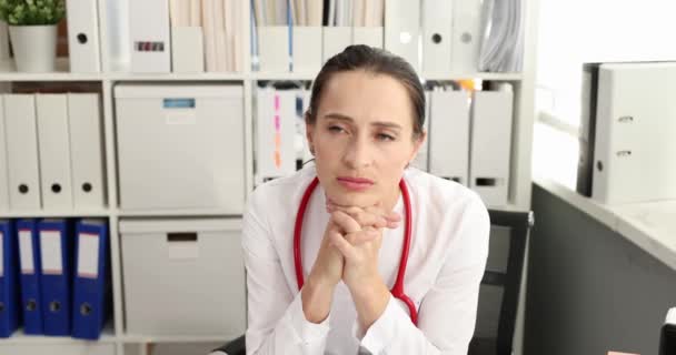 Mujer triste médico con estetoscopio en el cuello sentado en la mesa en la clínica 4k película — Vídeos de Stock