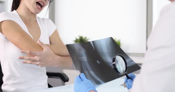 Médico examinando rayos X de la mujer dolor de codo en la clínica 4k película — Vídeo de stock