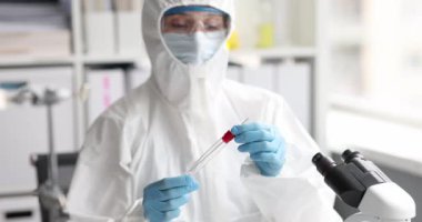 Koruyucu giysili ve solunum cihazlı doktor laboratuvar 4K filminde test tüpünden pamuk örneği alıyor.