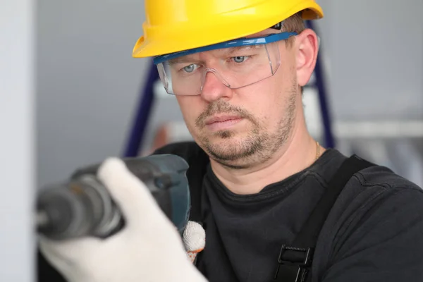 Mężczyzna w kasku budowlanym i okularach wierci ścianę — Zdjęcie stockowe