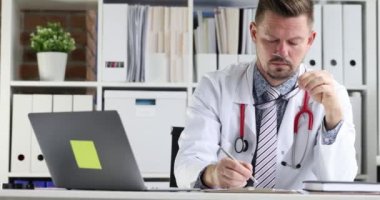 Genç doktor, iş yerindeki yavaş çekim 4K filminde hastanın tıbbi bilgilerini karta yazar.