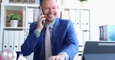 Takım elbiseli genç adam cep telefonuyla konuşuyor ve dijital tablette haberleri izledikten sonra seviniyor.