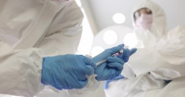 Koruyucu kıyafetli doktor cam şişeden şırıngaya ilacı çekiyor. 4K 'lık yakın çekim filmi yavaş çekim.