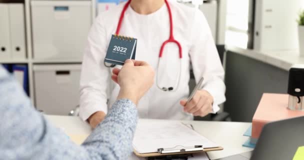 Paciente dando sonriente calendario de escritorio médico para 2022 en la cita en la clínica 4k película cámara lenta — Vídeo de stock