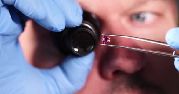 Jeweler looking at magnifying glass at pink diamond on tweezers closeup 4k movie slow motion — Stock Video