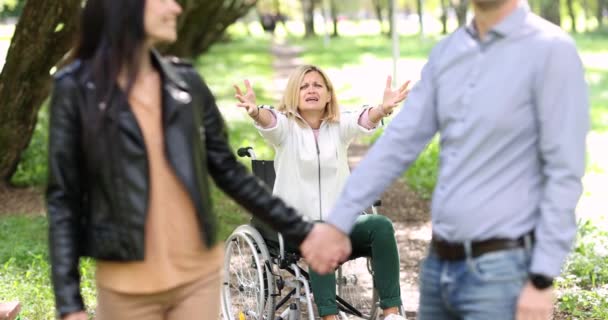 Vrouw in rolstoel schreeuwen op spoor van paar verlaten in de voorkant van haar in park 4k film slow motion — Stockvideo