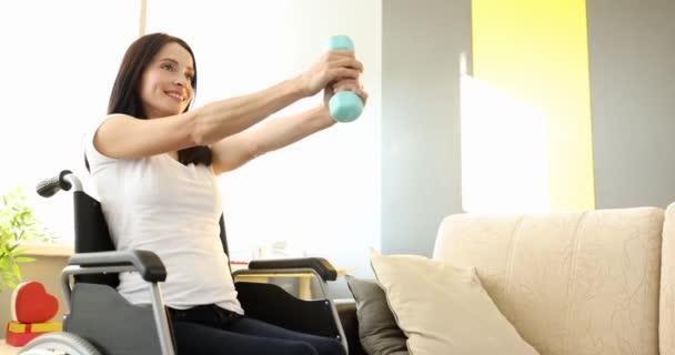 Mosolygó nő csinál kéz gyakorlatok súlyzókkal, miközben ül tolószékben lassított felvétel 4K film — Stock videók