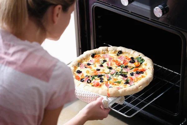 厨房里的女人在烤箱里烤披萨 — 图库照片