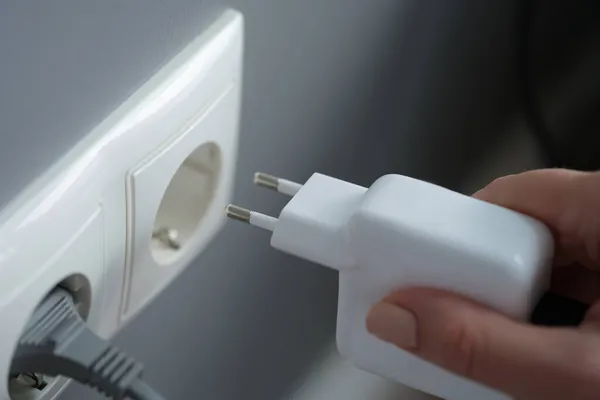 Hands plugging the charger into an outlet in the wall, close-up — Stock Photo, Image