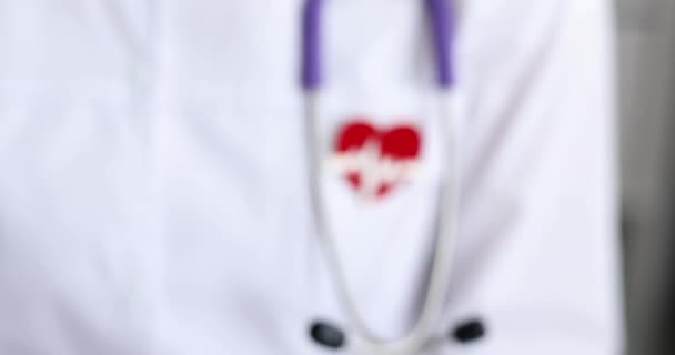 Doktor göğsüne asılı kalp elektrokardiyogramı şeklinde kırmızı bir ikon. 4K yakın çekim filmi. — Stok video