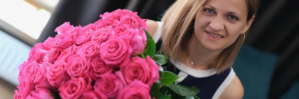 Young woman sitting on sofa and holding large bouquet of roses — Stock Photo, Image