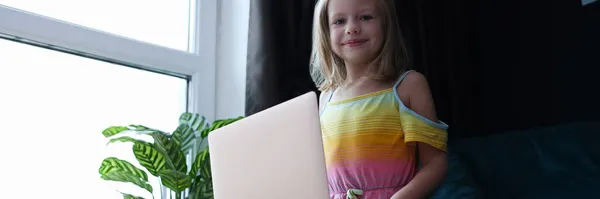 Klein meisje zit op de bank en houdt laptop vast — Stockfoto