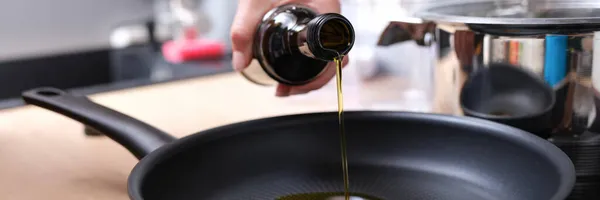 Vrouw giet olijfolie in hete koekenpan closeup — Stockfoto