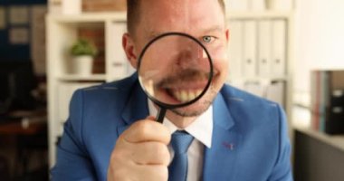 Genç gülümseyen işadamının portresi büyüteçle yavaş çekim 4K film izliyor.