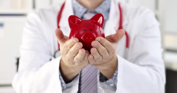 Mladý usměvavý lékař drží prasátko banka v ruce zpomalený film 4k — Stock video