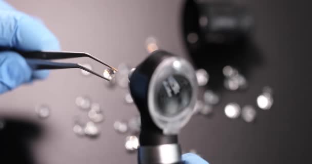 Handschoen juwelier houdt pincet met edelsteen en onderzoekt door vergrootglas slow motion 4k film — Stockvideo