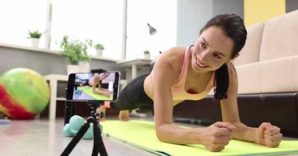 Souriant jeune femme se tient dans la planche sur le tapis et regarde l'écran du smartphone au ralenti film 4k — Video