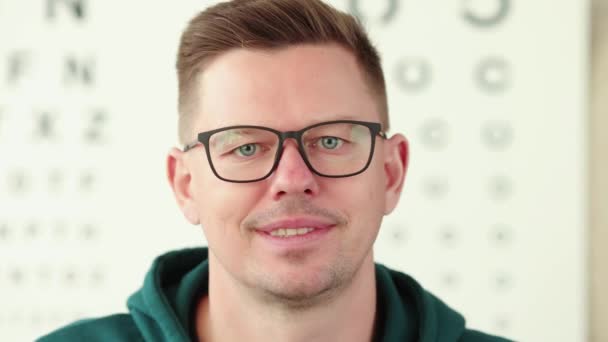 Jonge glimlachende man neemt af zijn bril in de achtergrond van oftalmische tafel slow motion 4k film — Stockvideo