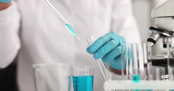 Ученый в перчатках из пипетки капает голубую жидкость в пробирку в лабораторной замедленной съемке 4k фильма — стоковое видео