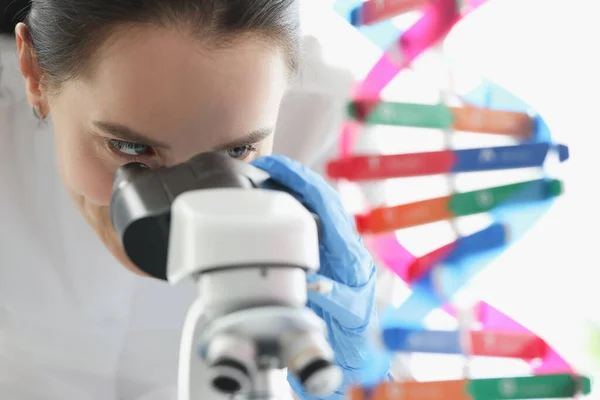 Mulher cientista olhando através de microscópio perto de mockup molécula de dna em laboratório — Fotografia de Stock